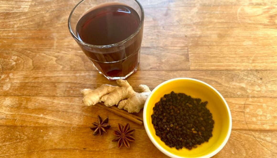 Holundertee im Glas mit Holunderbeeren, Zimtstange, Sternanis und Ingwer