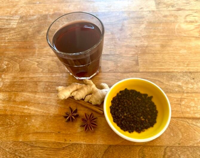 Holundertee im Glas mit Holunderbeeren, Zimtstange, Sternanis und Ingwer